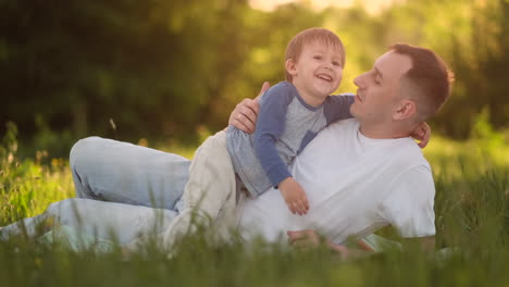 Loving-father-and-son-hugging-on-the-grass-at-sunset-in-slow-motion.